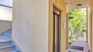 Un pasillo con una escalera a la izquierda y una puerta que da a un área exterior con árboles y una valla.