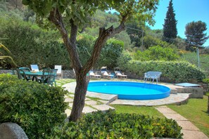 Ein Swimmingpool mit Liegestühlen und einem Tisch, umgeben von Grünflächen und Steinwegen.