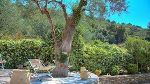 A stone table with two large pots and a folding chair in a garden with a stone wall and a tree.