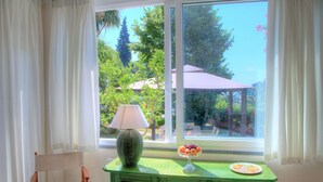 A room with a window, a green table with a lamp and fruit bowl, and a chair.