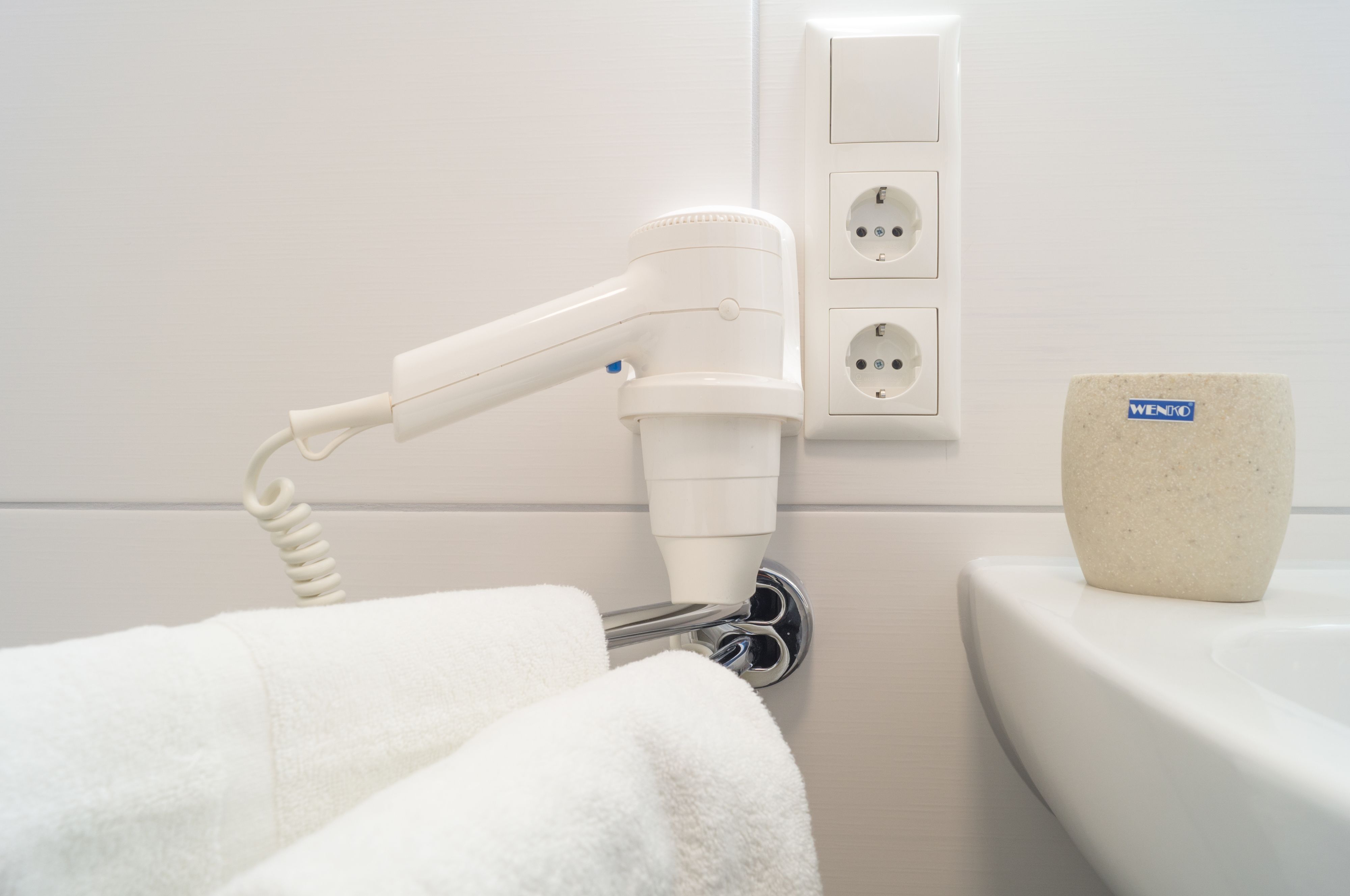 Ein Badezimmer mit einem an der Wand befestigten Föhn, einem Handtuchhalter und einem Waschbecken mit einem Steinglas auf der Ablagefläche.
