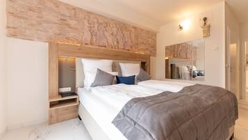 A modern bedroom with a large bed, a wooden headboard, and a stone wall with carvings.