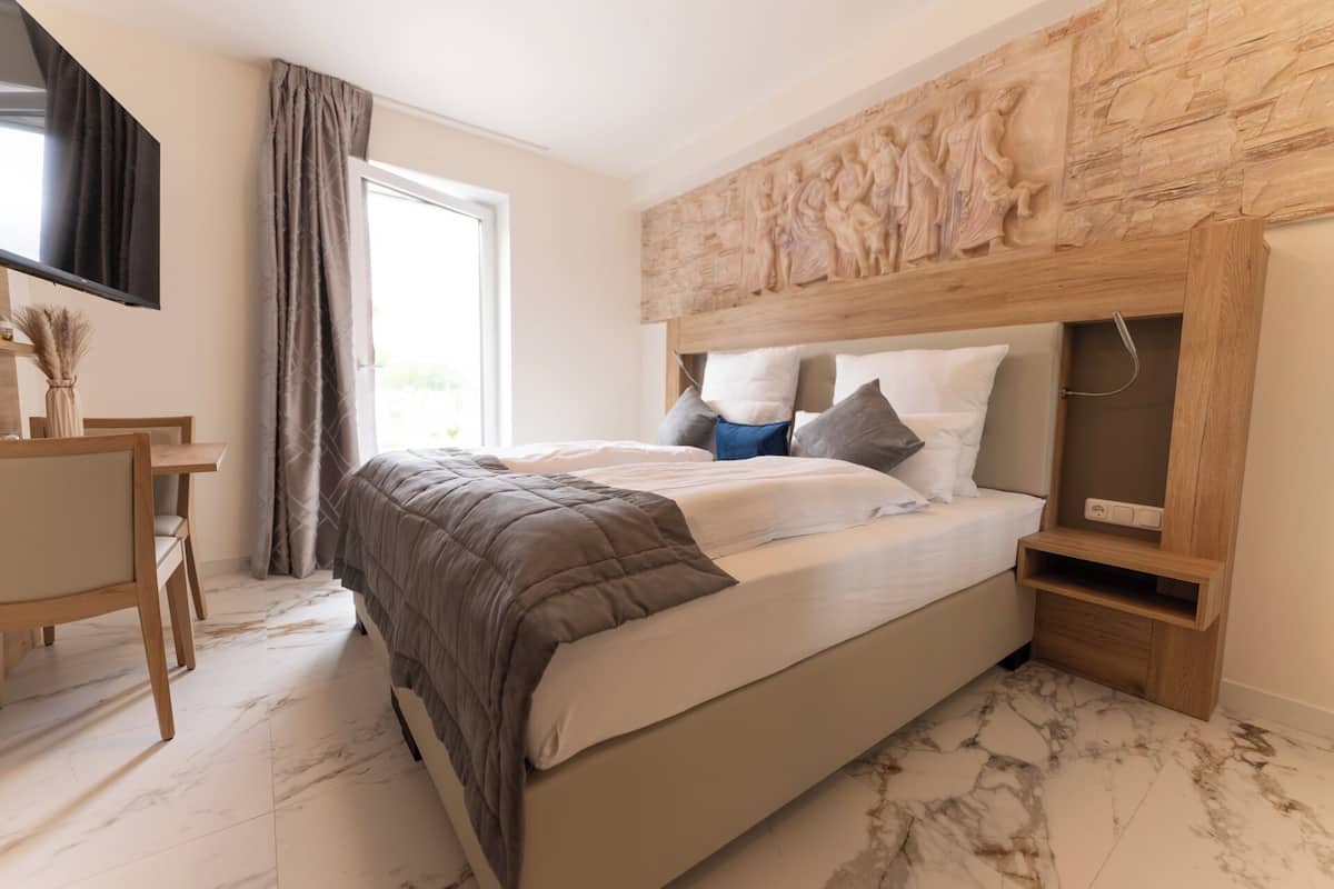 A modern bedroom with a marble floor, a bed with a wooden headboard, a bedside table, and a large window with curtains.