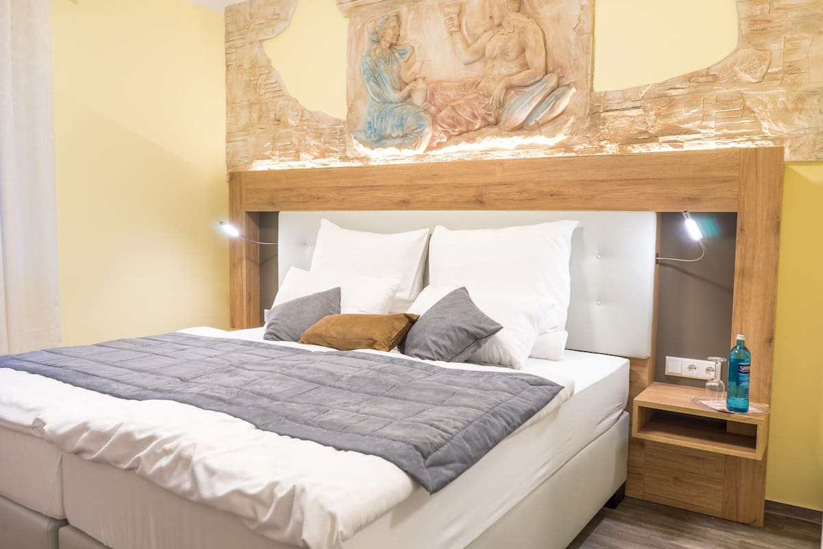A bed with a wooden headboard, white and gray pillows, a gray blanket, and a nightstand with a bottle and glass.