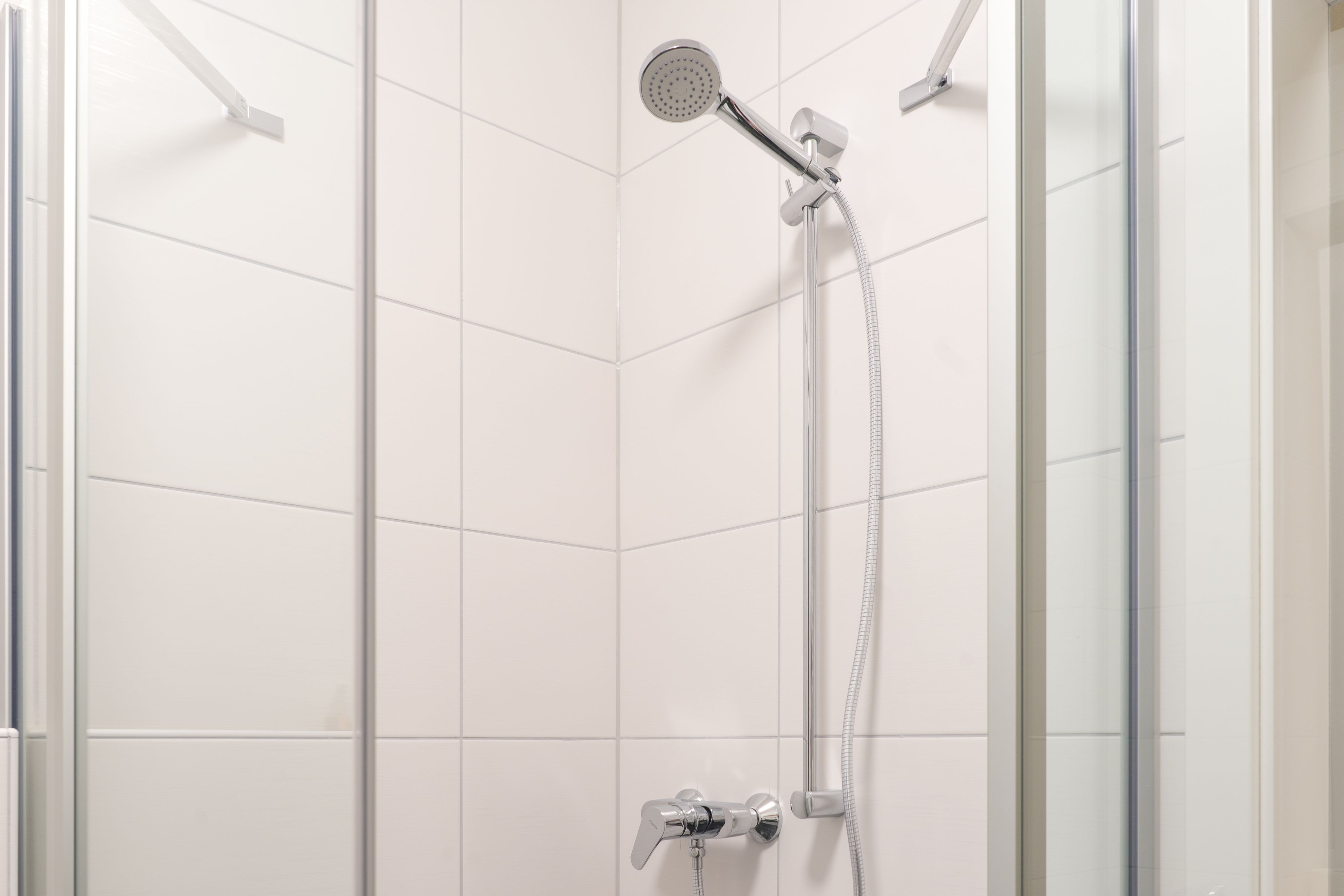 Una ducha moderna con cabezal de ducha manual y llave de control en la pared.