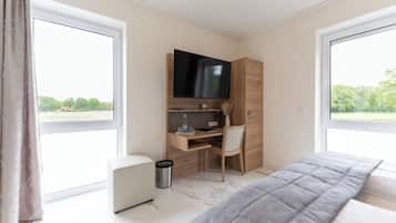 A bedroom with a bed, a desk with a chair, a TV, and a window with a view of greenery.