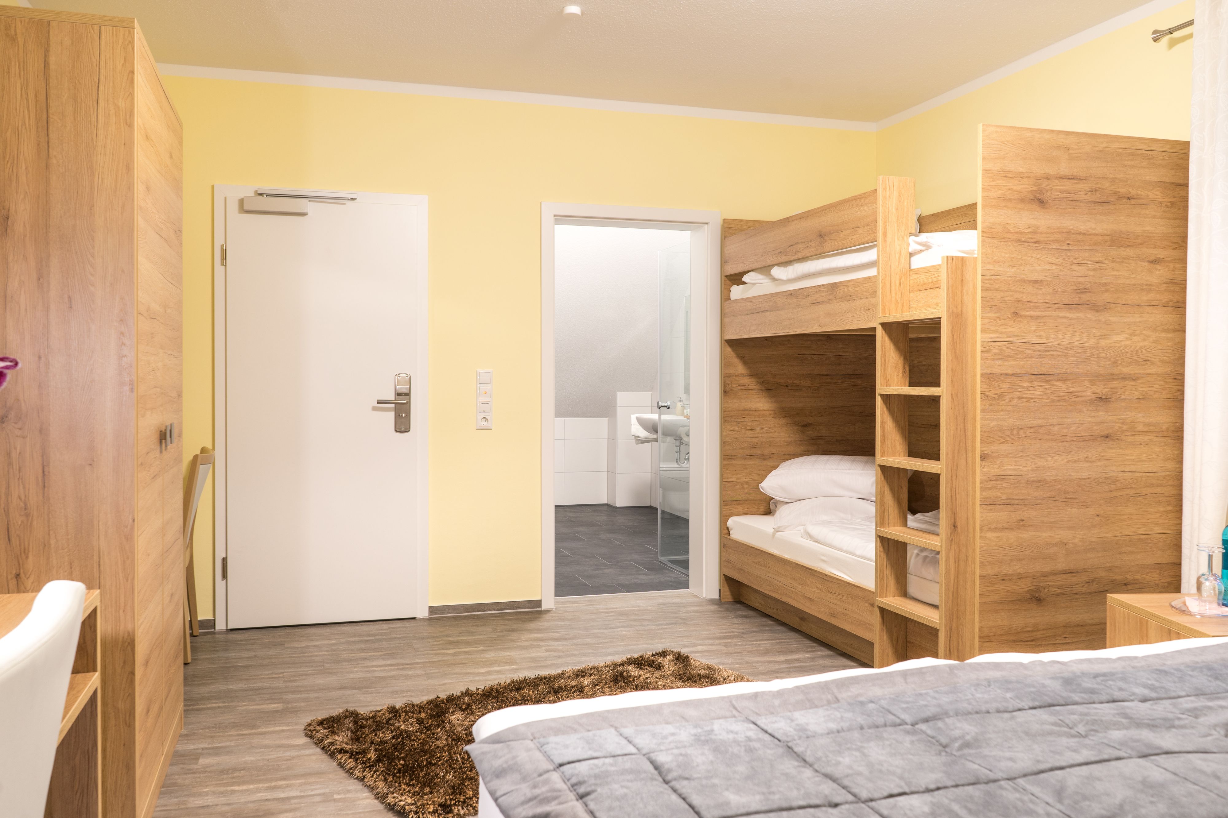 A bedroom with a bunk bed, a desk, and a bathroom visible through an open door.