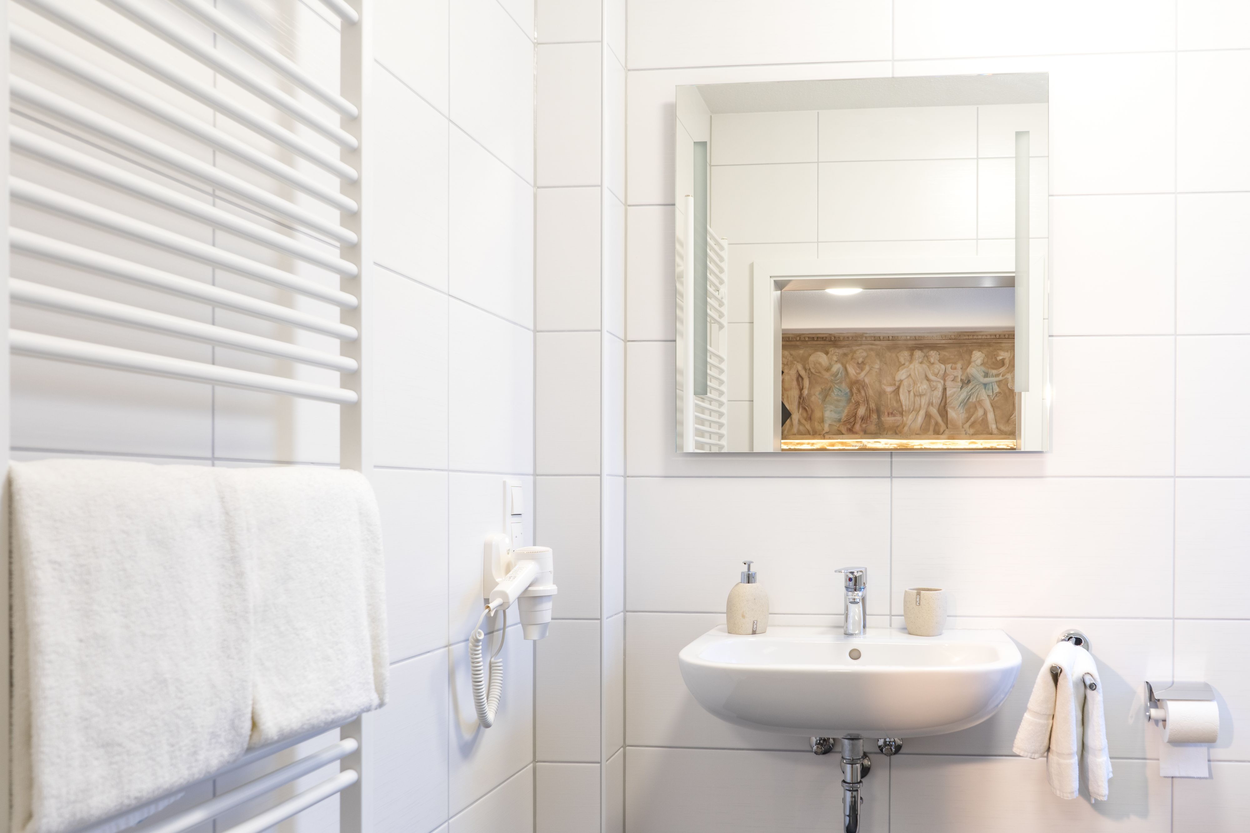 A bathroom with a white sink, a towel rack, a mirror, and a wall-mounted heater.
