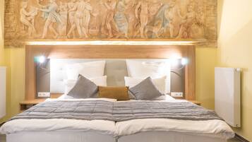 Ein Hotelzimmer mit einem großen Bett, einem Kopfteil mit klassischer Reliefverzierung und einem Nachttisch mit einer Lampe.
