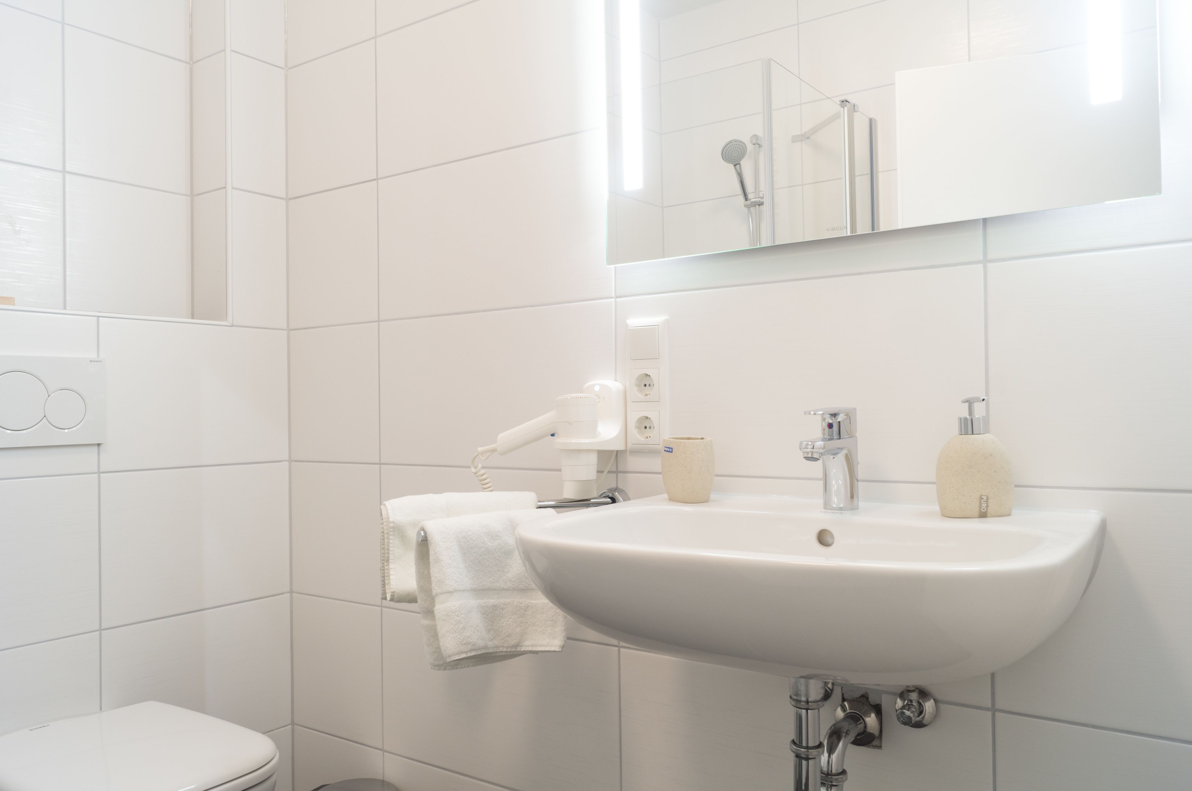 Un baño moderno con lavamanos, espejo y retrete blancos.