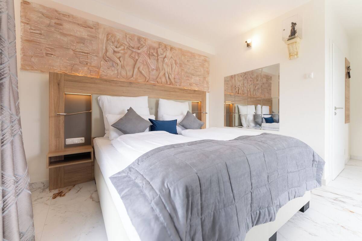 A modern bedroom with a large bed, a wooden headboard, and a mirror.