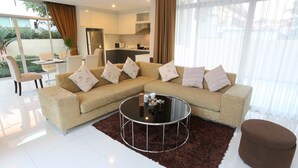 A modern living room with a sectional sofa, a round coffee table, and a brown ottoman. - AnB Pool Villa 3BR Glass House in Pattaya (Sattahip)
