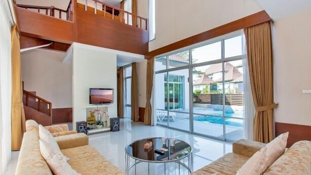 A spacious living area with a high ceiling, a large window, and a staircase leading to an upper level. - AnB Pool Villa 3BR Glass House in Pattaya (Sattahip)