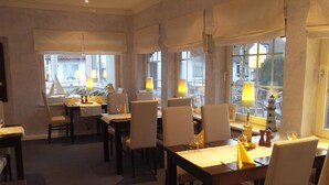 Un espace repas avec des tables et des chaises, de grandes fenêtres et une vue sur l’extérieur.