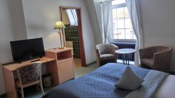 A hotel room with a bed, a desk with a television, a chair, and a small table.