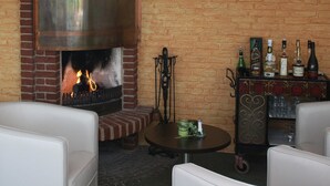 Un espace intérieur accueillant avec un coin salon, une cheminée en briques, un bar où sont exposées différentes bouteilles, et une table ronde sur laquelle se trouve un objet vert.