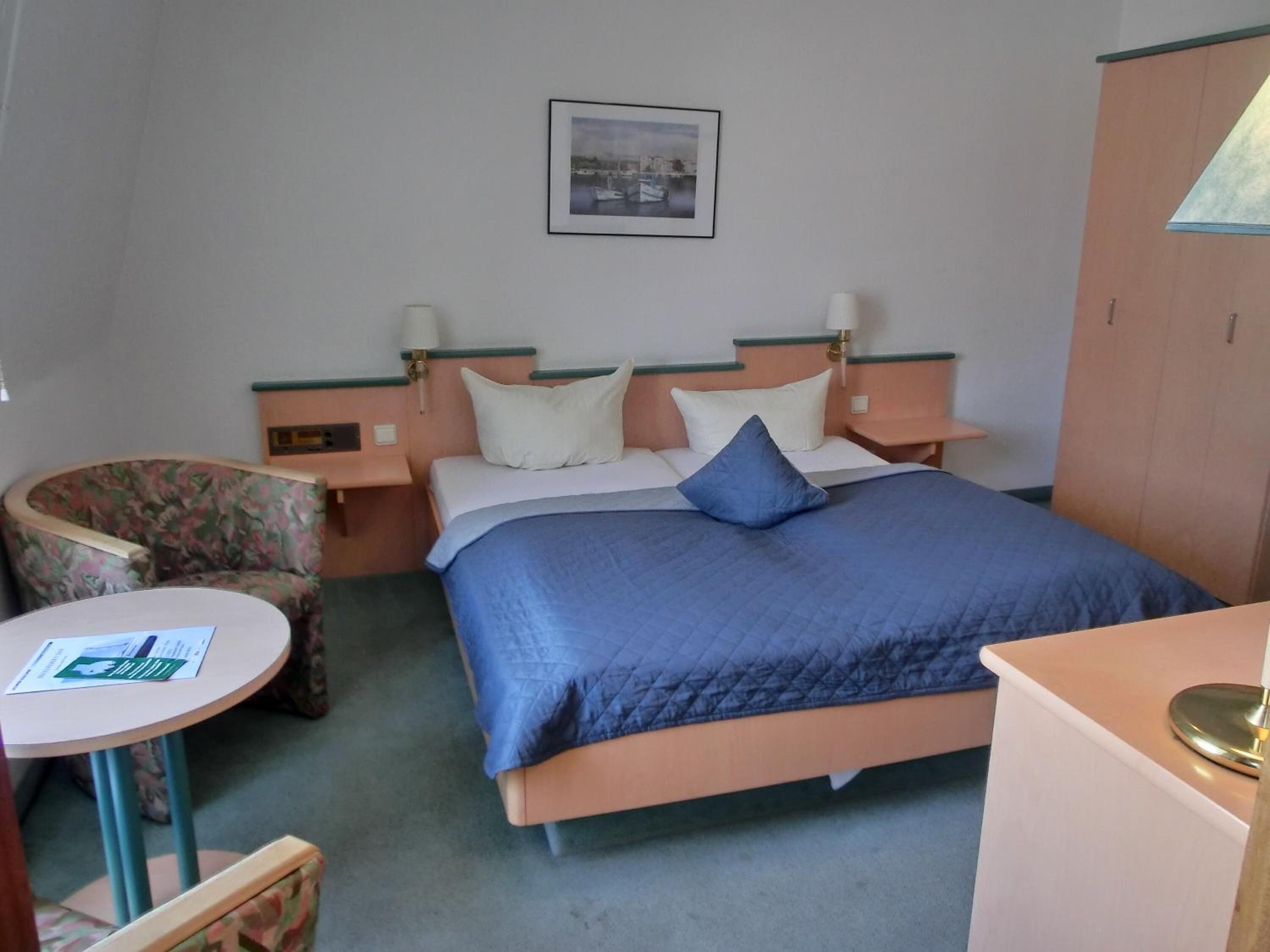A hotel room with a bed, two bedside tables, a chair, a small table, and a wardrobe.