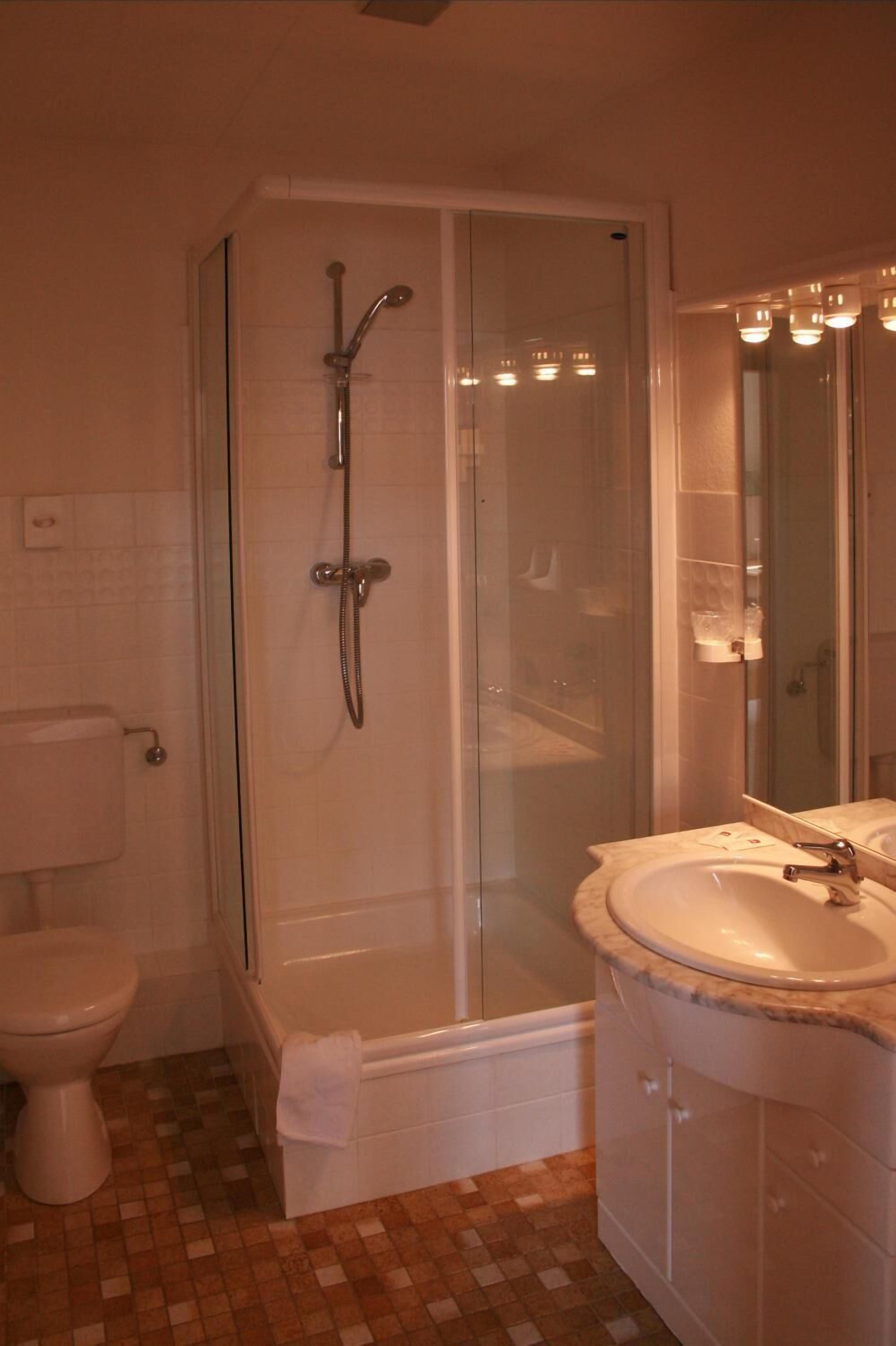 Un baño con ducha de vidrio, inodoro y lavamanos con espejo.