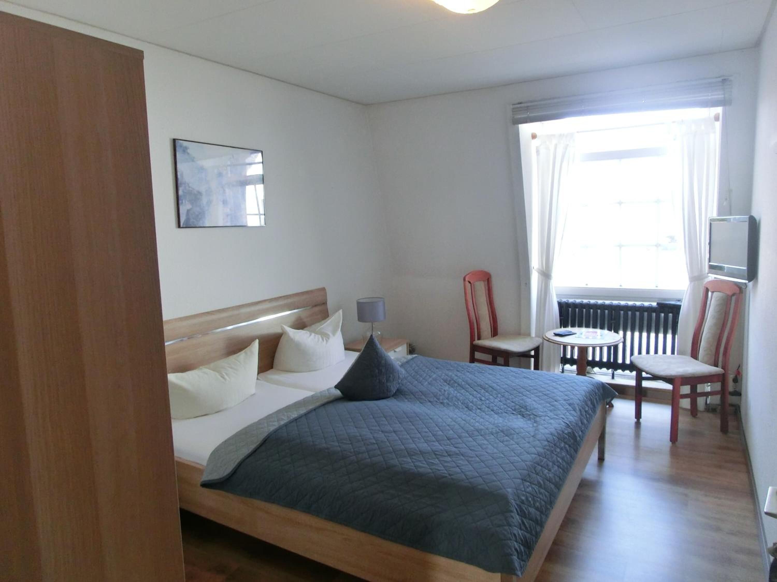 A bedroom with a bed, a chair, a table, and a TV.