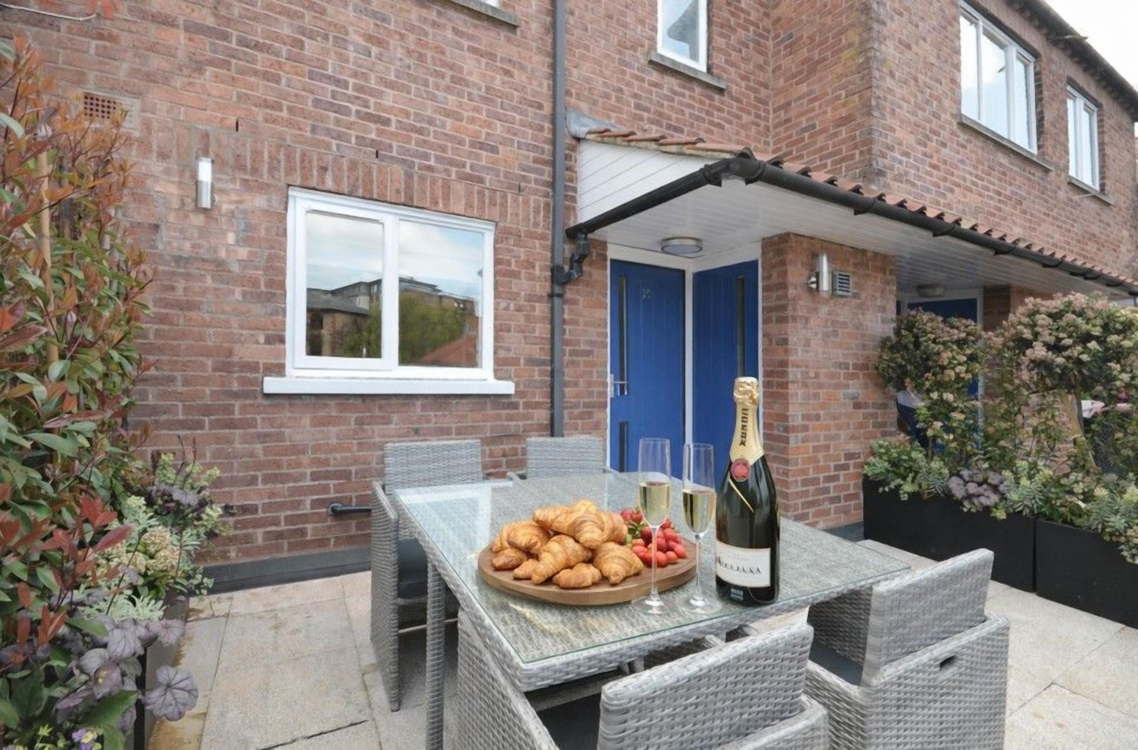 A patio with a table set for a meal, a bottle of champagne, and a plate of croissants.