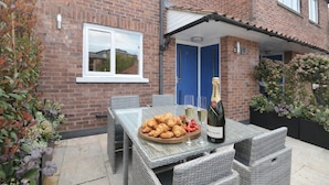 Un patio con una mesa dispuesta para una comida, una botella de champán y un plato de croissants.
