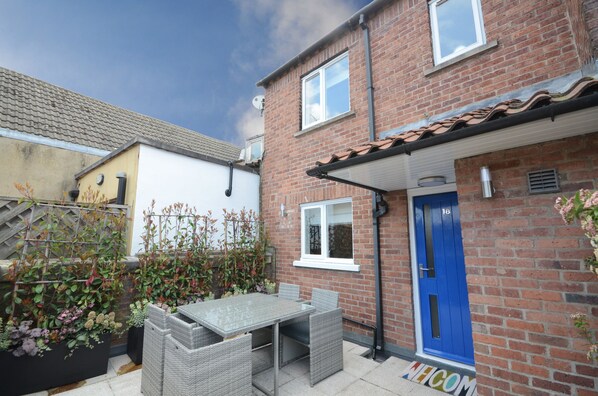 A residential property with a patio area featuring a table and chairs, a blue door, and a brick exterior.