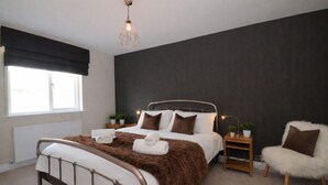 Un dormitorio moderno con cama, mesitas de noche, una silla y un ventanal.