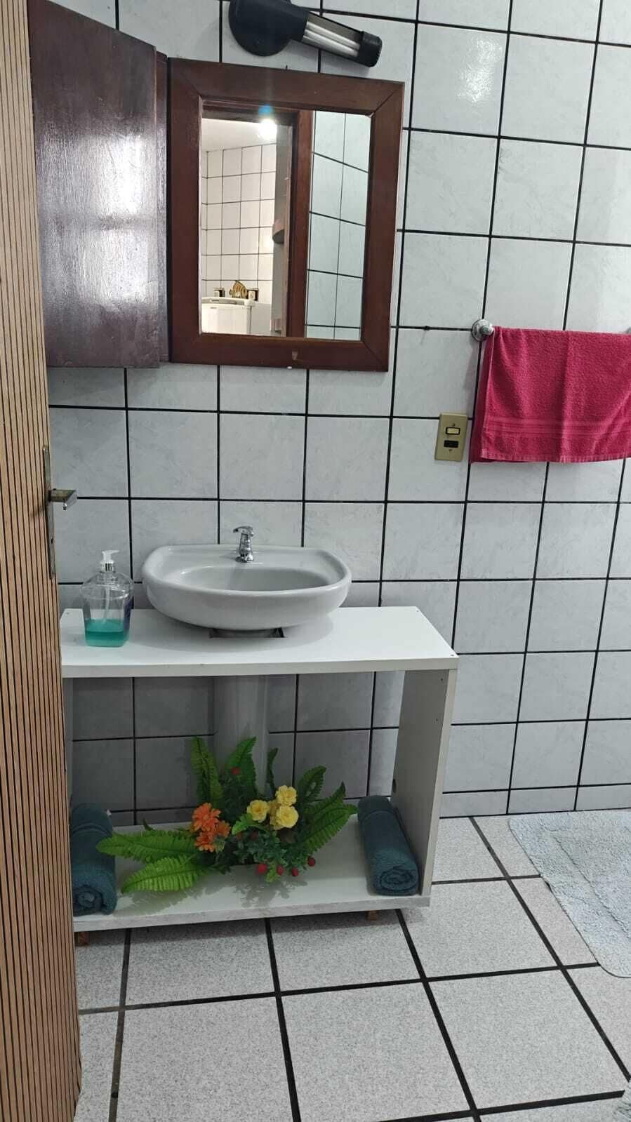 Une salle de bain avec un lavabo blanc, un miroir et une serviette rouge accrochée au mur.