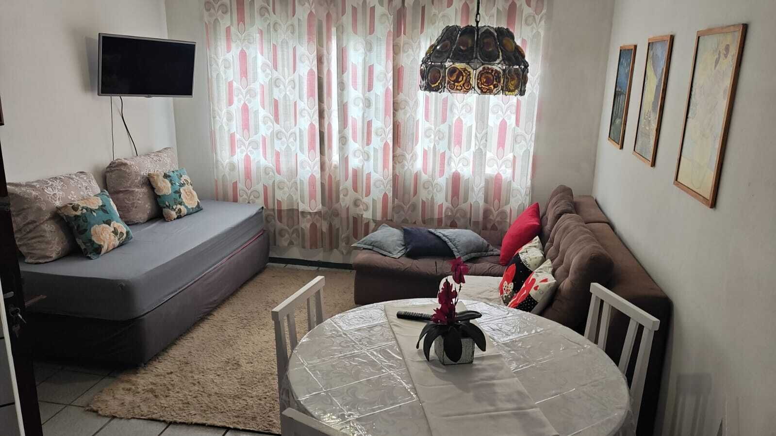 En stue med sofa, spisebord, fjernsyn og et mønstret gardin.