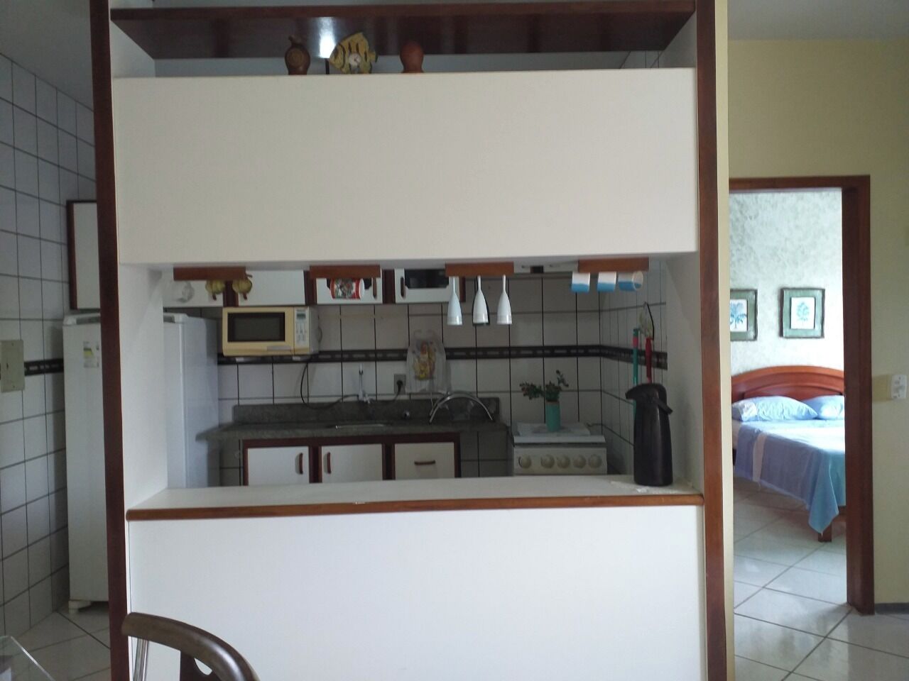 Una cucina compatta con forno a microonde, lavello e mobili. Si intravede un letto nella stanza adiacente.