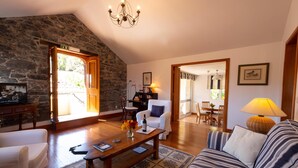 A cozy living room with a stone wall, a wooden ceiling, a chandelier, a sofa, a coffee table, and a dining area in the background.