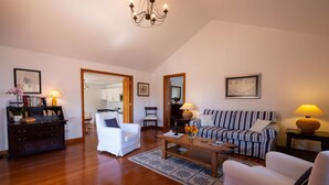 A spacious living room with a wooden floor, a white sofa, a striped sofa, a white armchair, a coffee table, and a bookshelf.