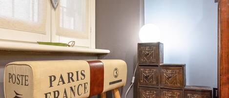 A vintage-style mailbox with "POSTE PARIS FRANCE" on it, wooden cabinets with geometric patterns, and a window with sheer curtains.