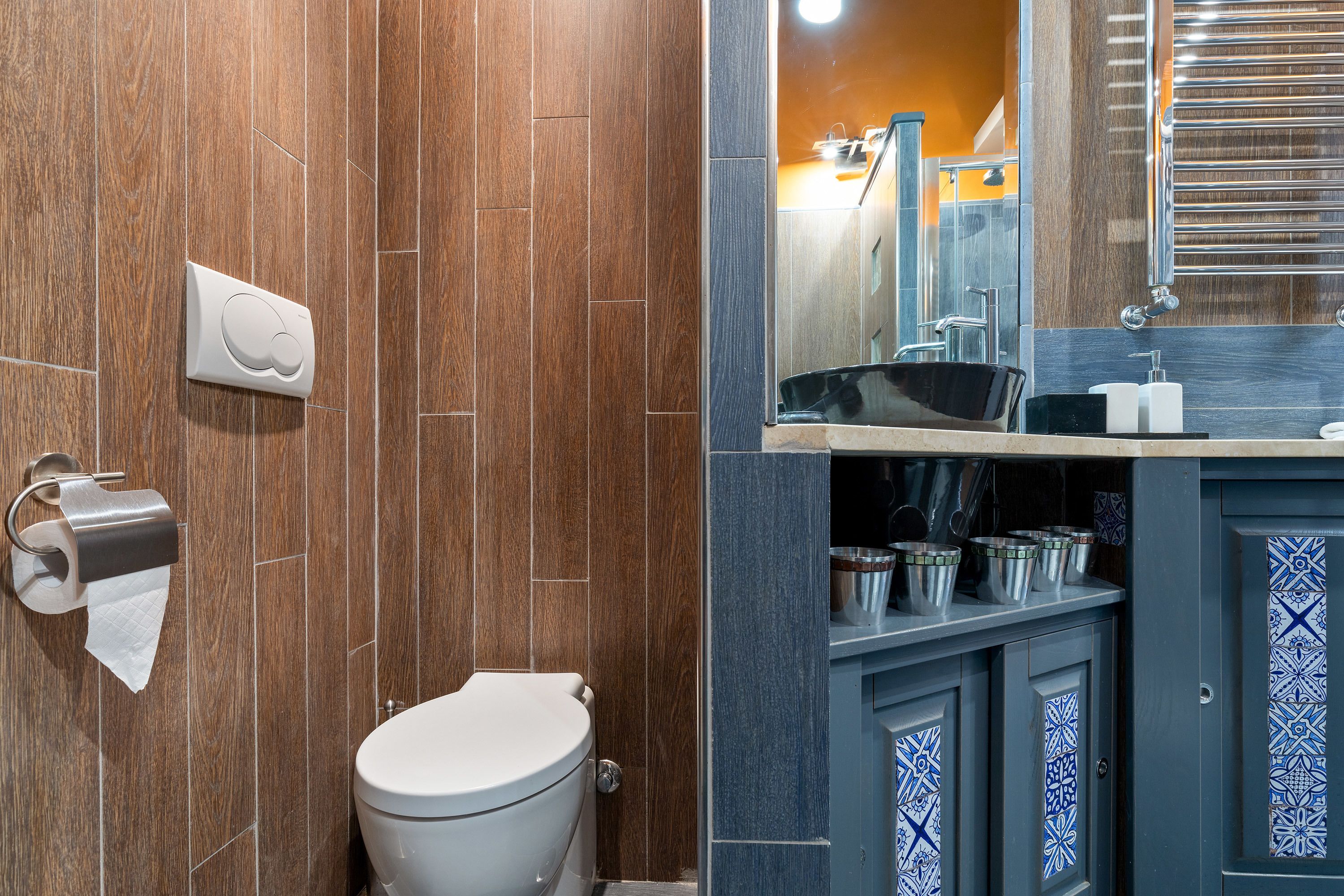 Ein Badezimmer mit Holzwand, Toilette, Waschbecken mit Spiegel und Handtuchspender.