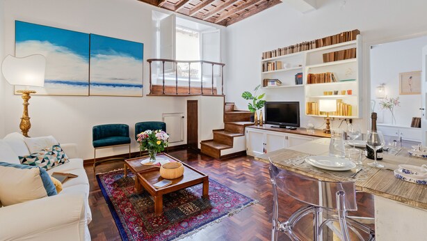 A spacious living area with a wooden ceiling, a large painting, a sofa, a coffee table, and a dining area with a TV and bookshelves. - Rome as you feel - Vetrina Apartment (Rome)