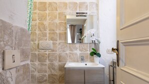 Een badkamer met een stenen muur, een witte wastafel, een spiegel en een toilet.