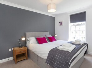 A bedroom with a bed, bedside table, lamp, and a window with blinds. - Fountains View 2 bedroom Apartment (York)