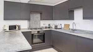 Una cocina moderna con gabinetes grises, horno empotrado, microondas, estufa a gas, pileta y tabla de cortar de madera.