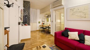 Un salon avec un canapé rouge, une table basse en bois et un coin repas comprenant une table et des chaises.