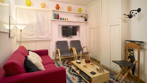 Un salon avec un canapé rouge, deux fauteuils gris, une table basse en bois et un téléviseur fixé au mur.