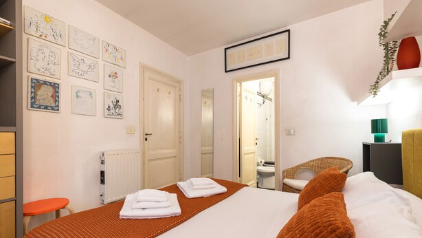 Une chambre d’hôtel avec un lit, des serviettes, des œuvres d’art accrochées au mur, un radiateur, une chaise et une table de chevet.