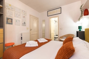 Une chambre d’hôtel avec un lit, des serviettes, des œuvres d’art accrochées au mur, un radiateur, une chaise et une table de chevet.
