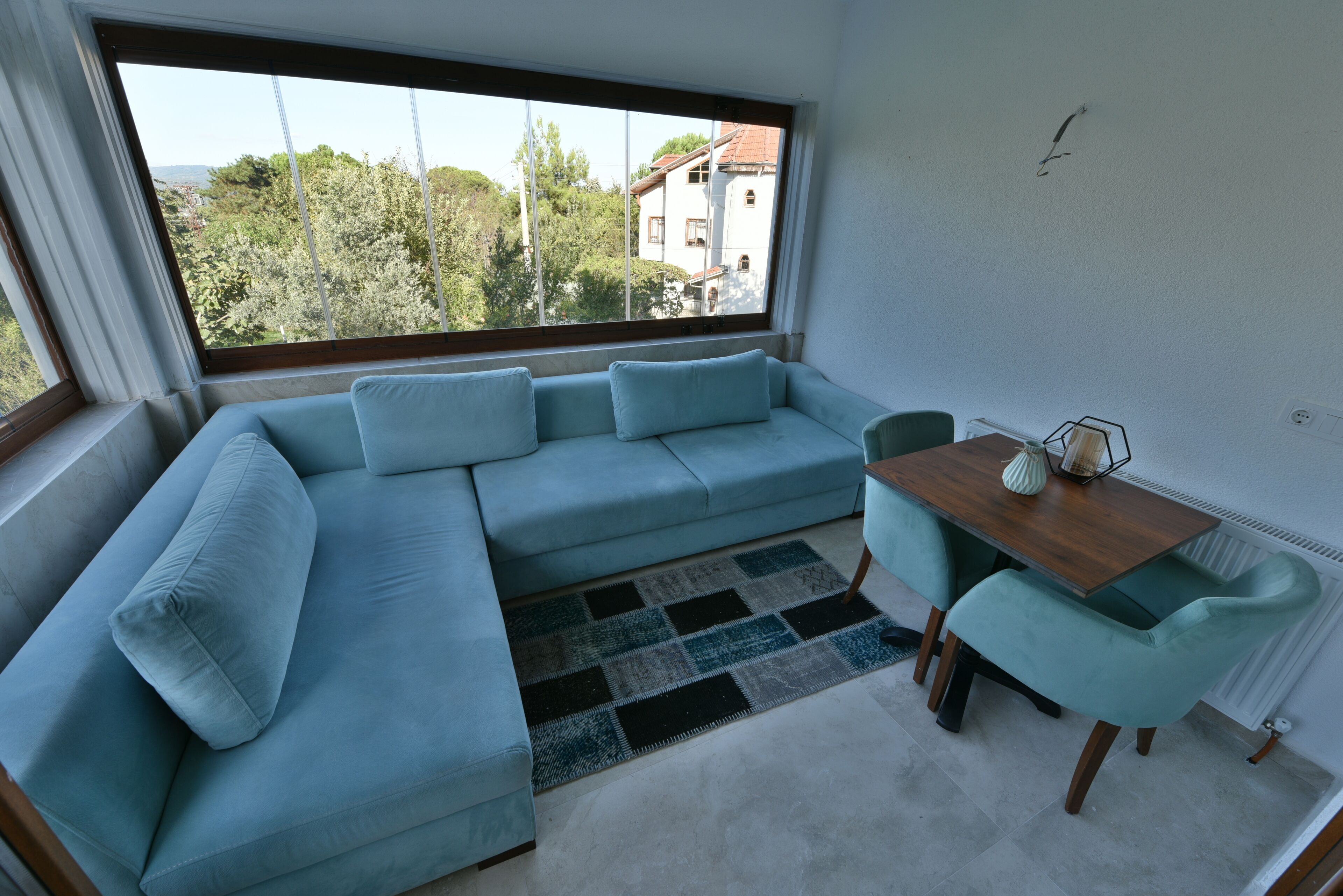 A modern living room with a light blue sectional sofa, a wooden dining table, and teal chairs.