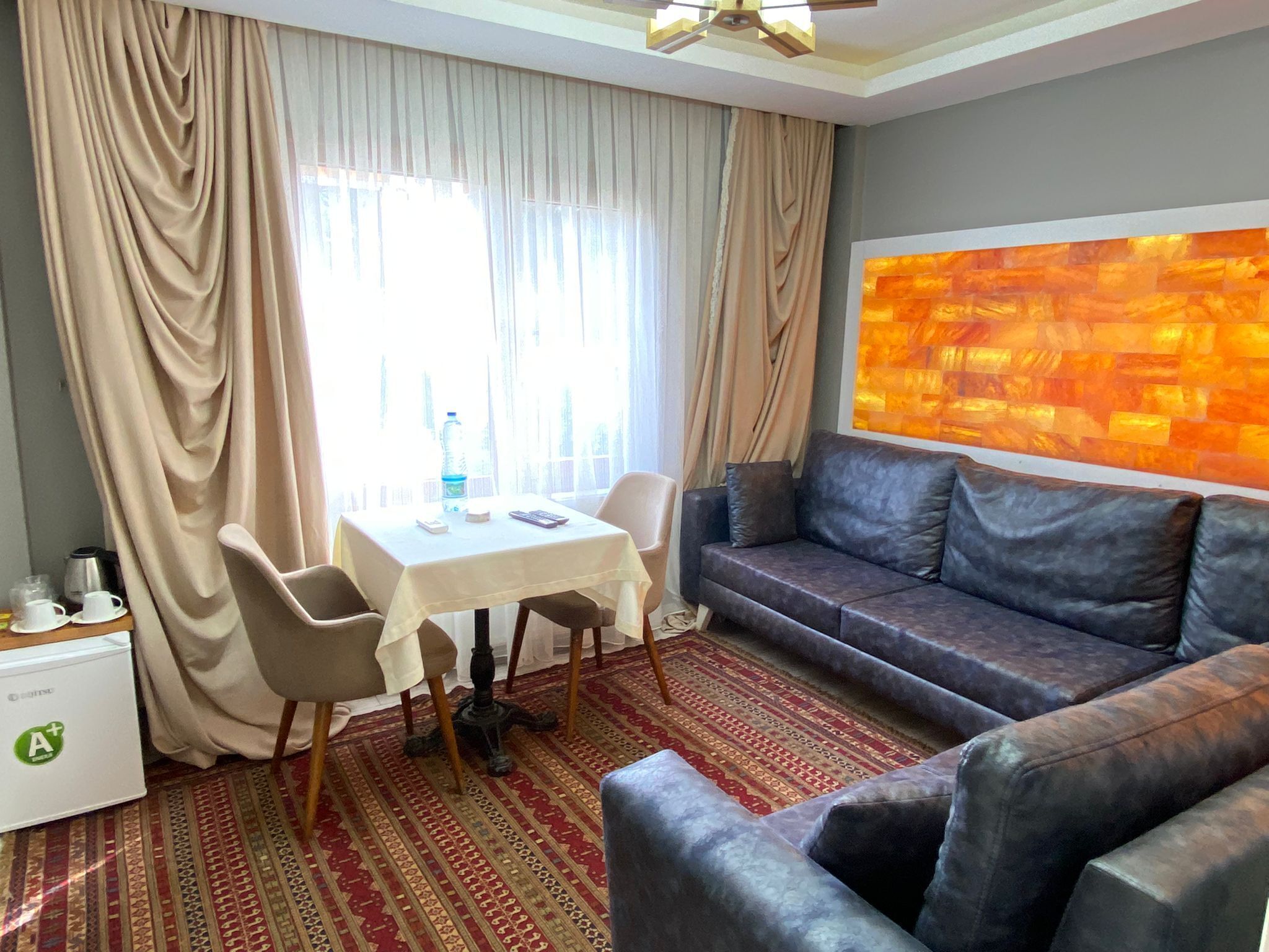 A hotel room with a sofa, a small table with chairs, a patterned rug, and a large abstract painting on the wall.