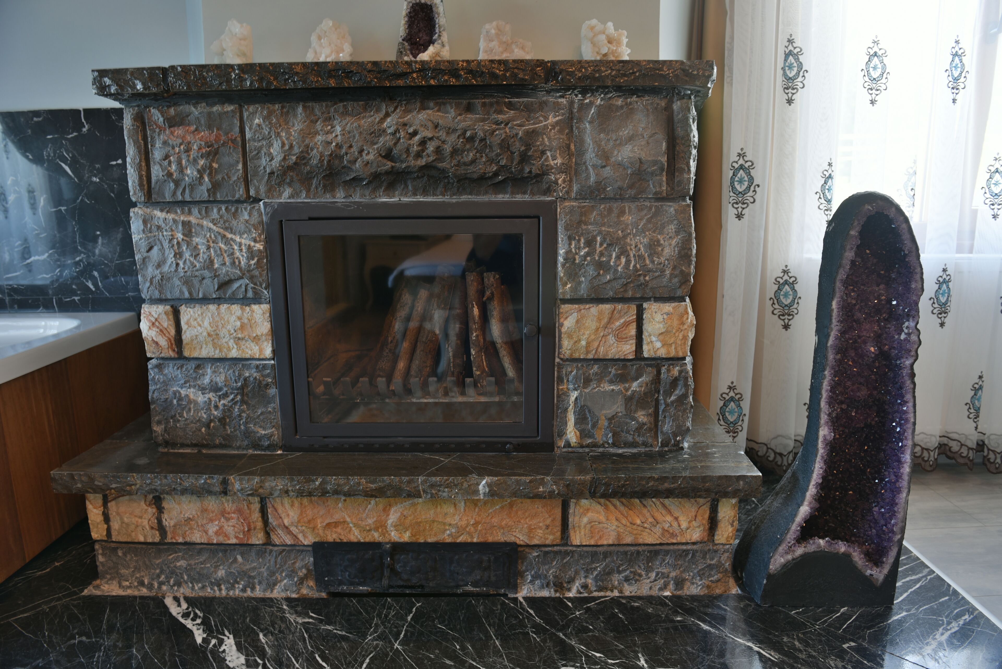 A stone fireplace with a glass door, surrounded by a marble floor.