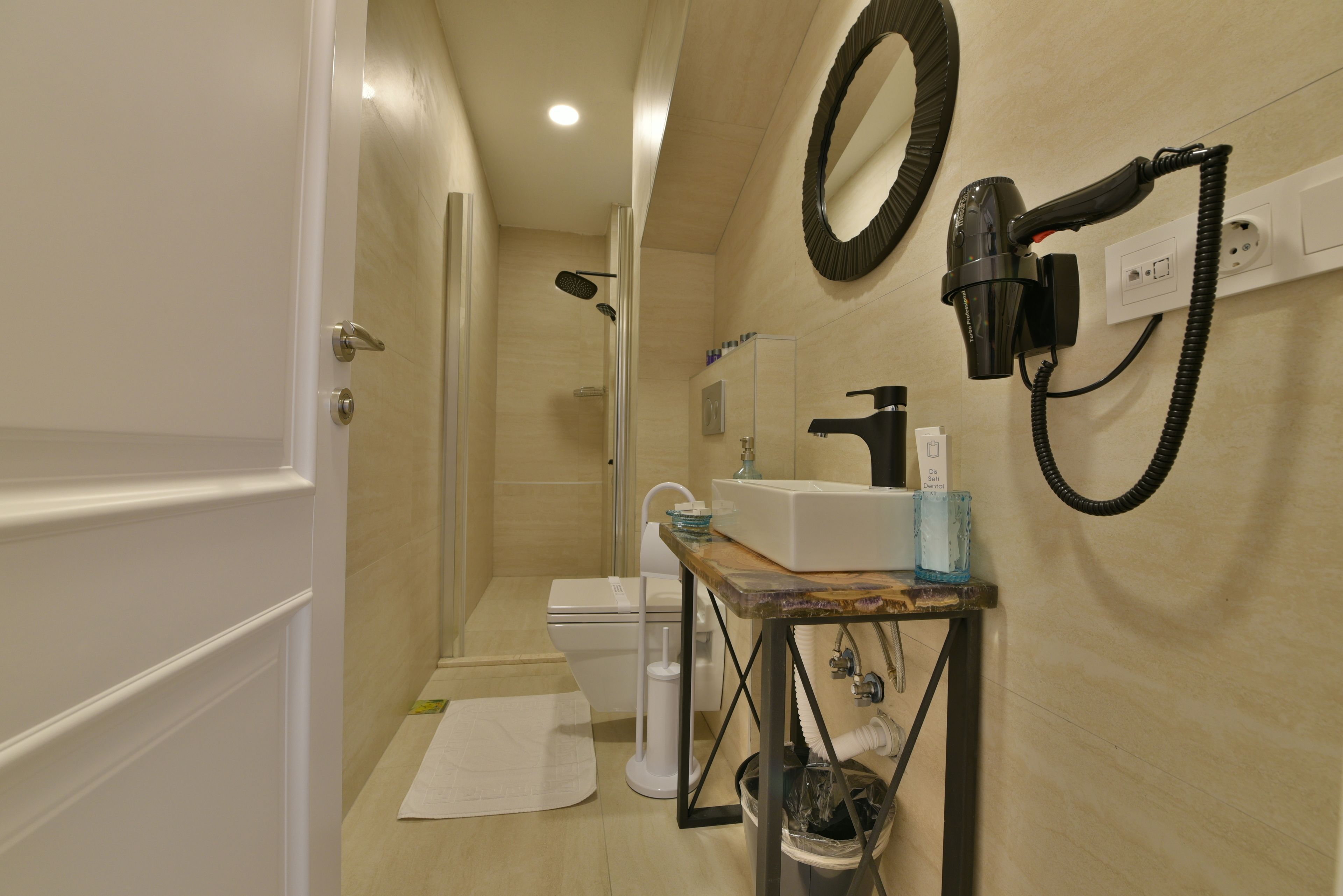 A bathroom with a shower, toilet, sink, and hairdryer mounted on the wall.