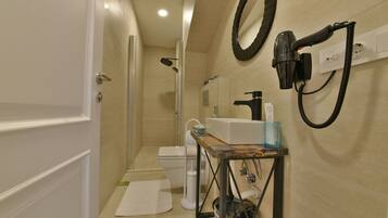 A bathroom with a shower, toilet, sink, and hairdryer mounted on the wall.