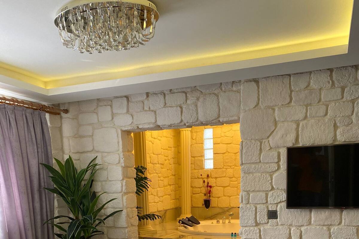 Habitación de hotel con una cama grande, un televisor montado en la pared, un muro de piedra y un baño con bañera y ducha.
