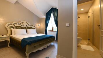 A bedroom with a large bed, a bedside table, a nightstand, a window with curtains, and a bathroom with a shower and toilet.