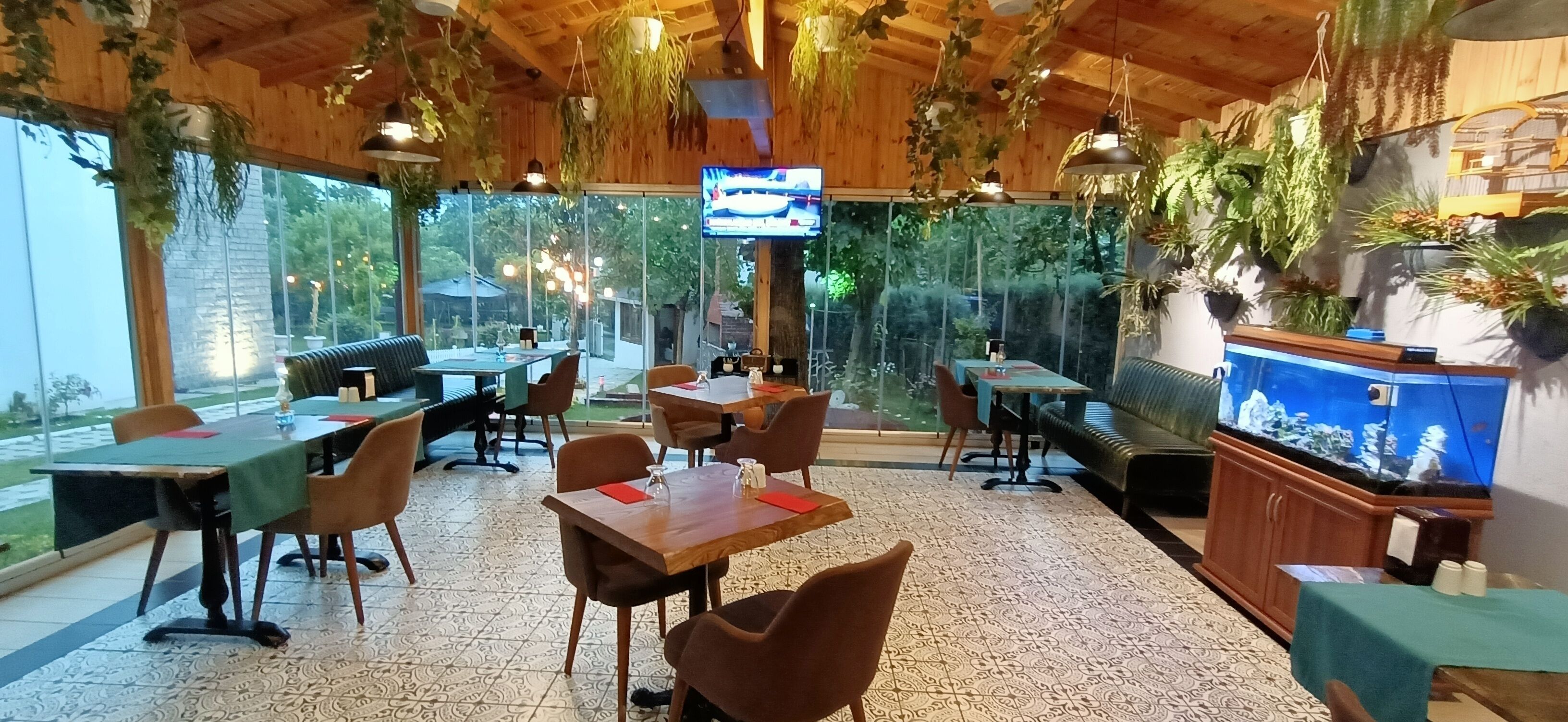 Un restaurante con techos de madera, plantas colgantes y un gran acuario. Mesas y sillas dispuestas para comer.